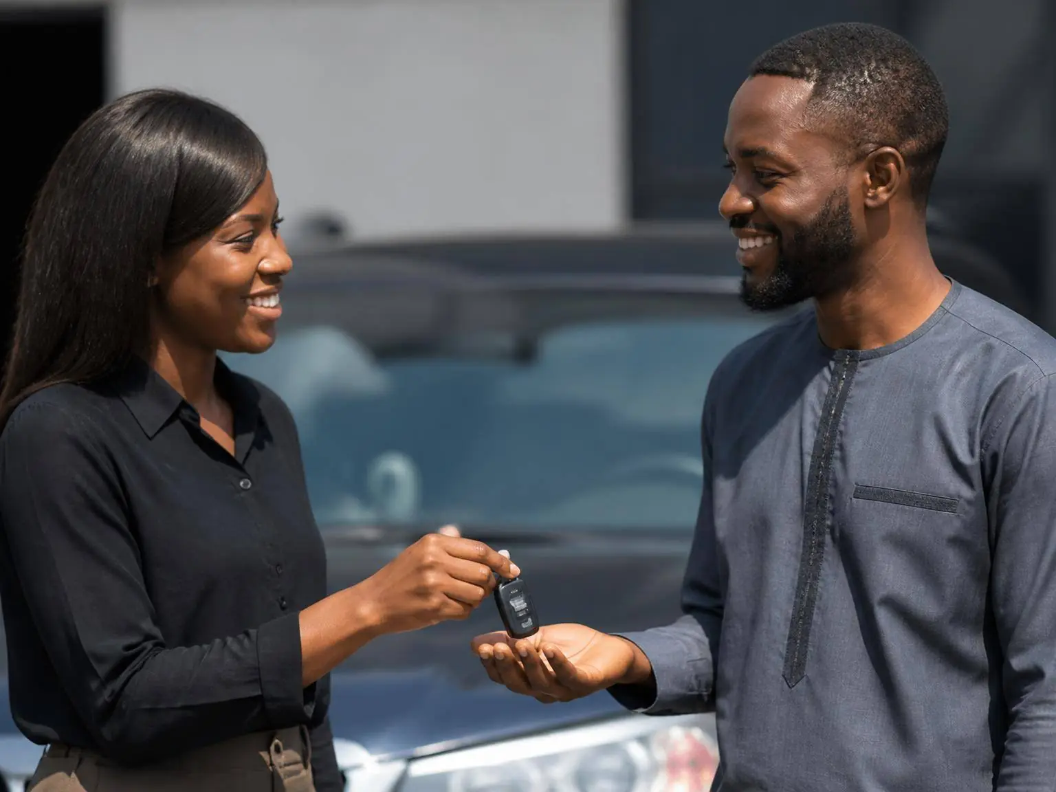 An Aare Auto sales representative handing a car key fob to a smiling customer in the dealership yard